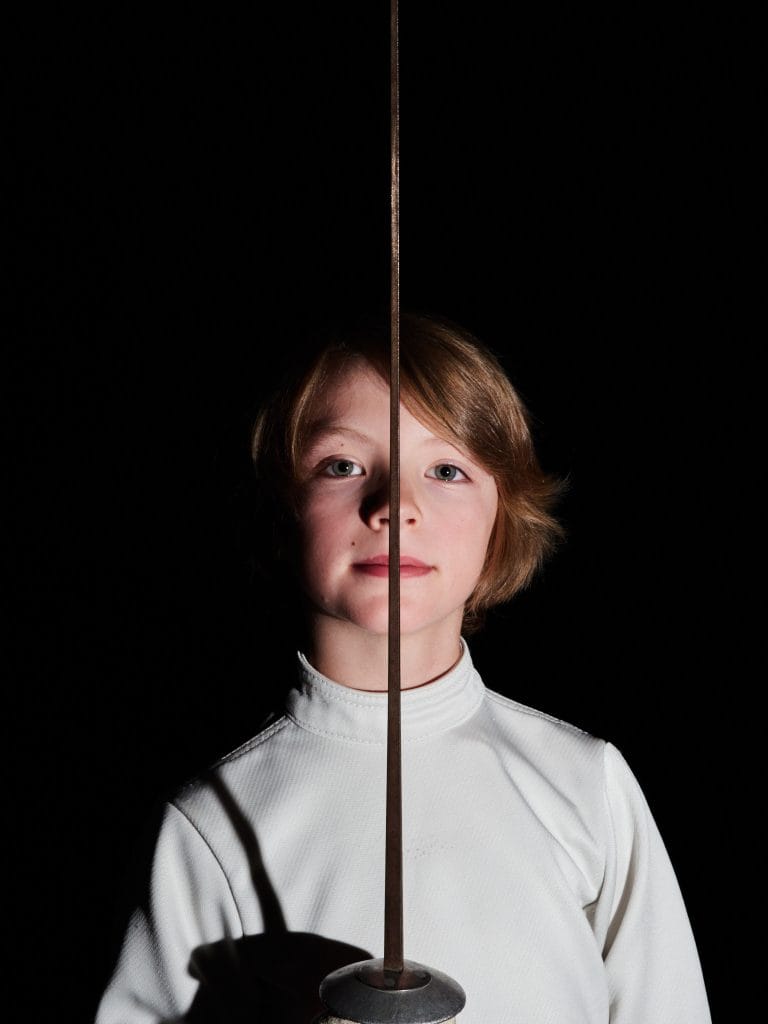 Portrait en studio de Gabriel, un jeune escrimeur. Il est de face et regarde l'objectif avec un regard déterminé. Son visage est éclairé de côté et une ombre est projetée sur l'autre moitié.