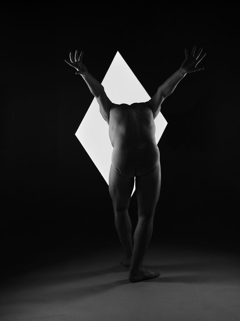 Valentin, danseur, dans une photographie artistique en studio, posant devant un losange de lumière, en noir et blanc.