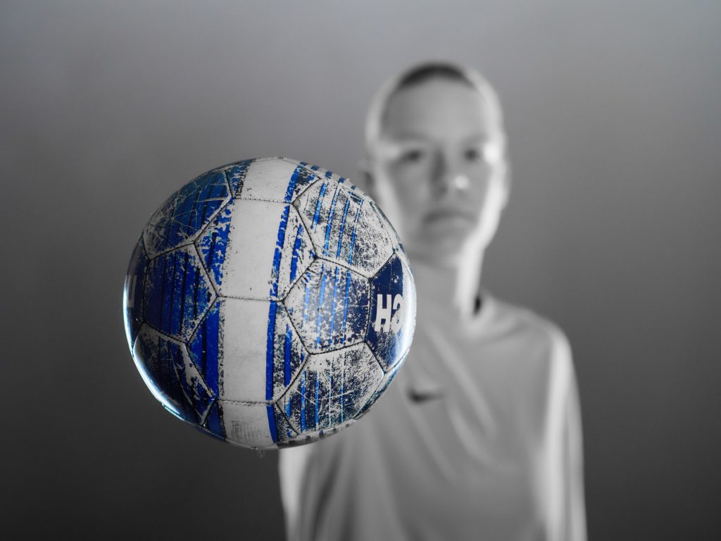 Portrait studio en noir et blanc de Wiktoria, une gardienne de foot, tenant un ballon de football bleu vers la caméra.