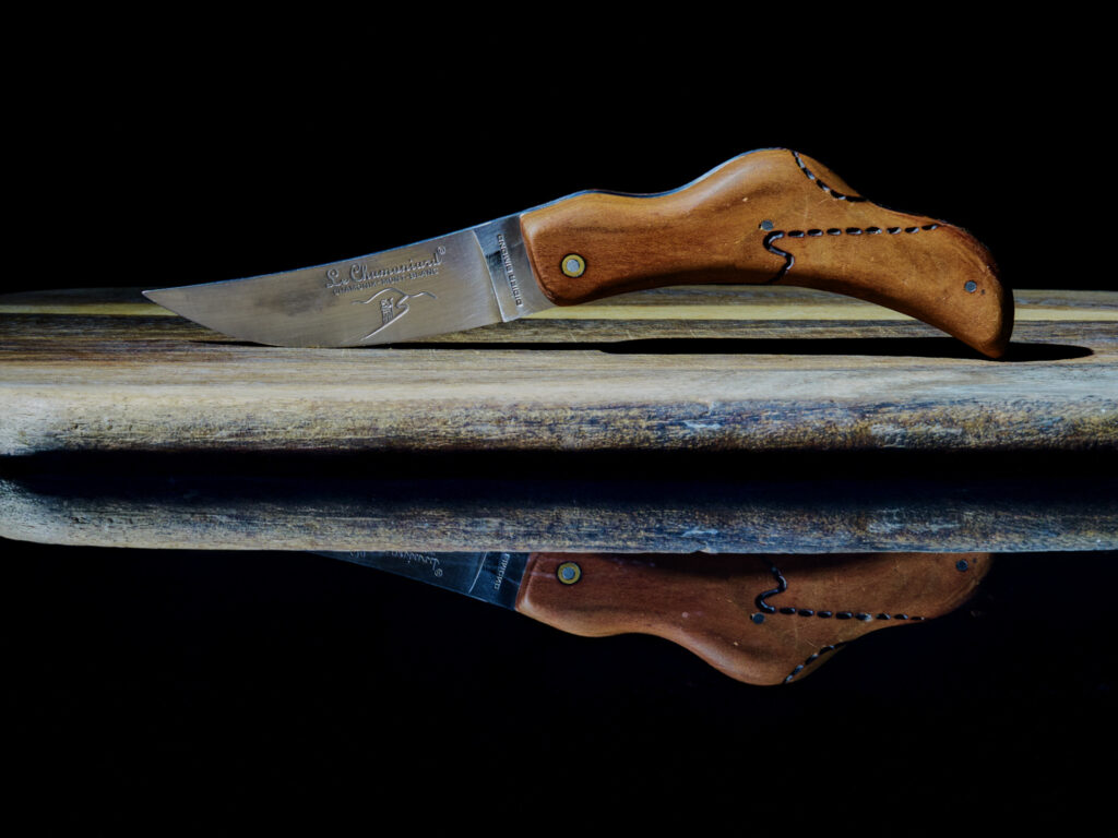 Couteau de poche pliant avec manche en bois foncé et lame en acier, posé sur une surface réfléchissante pour un effet miroir.