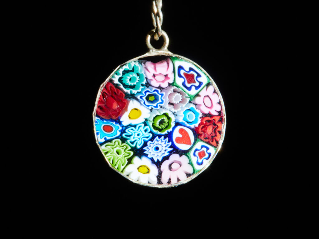 Gros plan sur un pendentif ovale Millefiori en verre de Murano aux motifs floraux colorés sur fond noir.