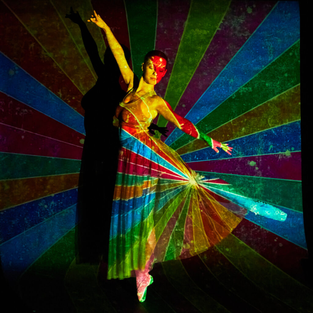 Danseuse artistique avec projection de motifs arc-en-ciel vifs et lumineux sur le corps et la robe.