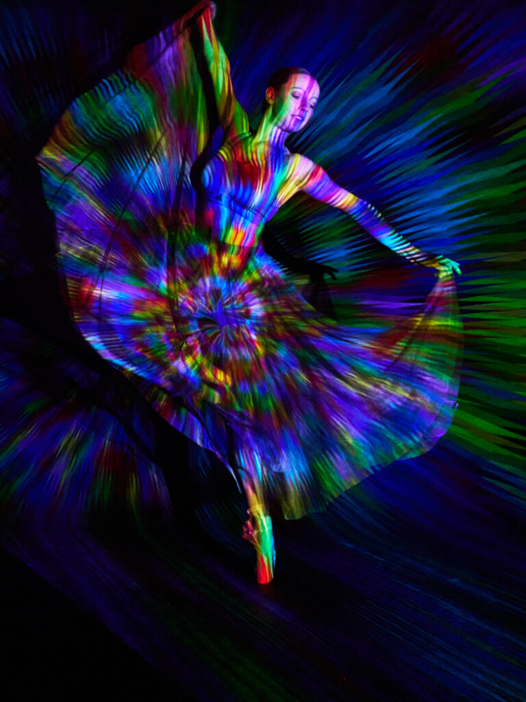 Danseuse en mouvement, baignée par une projection psychédélique de lumière tourbillonnante et vive.