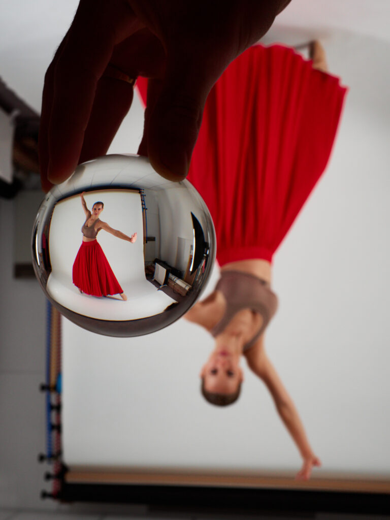 Danseuse vue à l'envers et déformée à travers une boule de cristal tenue en gros plan.