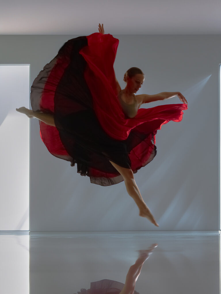 Danseuse en grand jeté, drapé rouge en mouvement, capturé en studio avec éclairage professionnel.