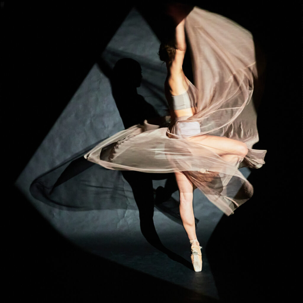 Danseuse en pointe, enveloppée dans un voile de tissu léger, capturée en mouvement aérien.