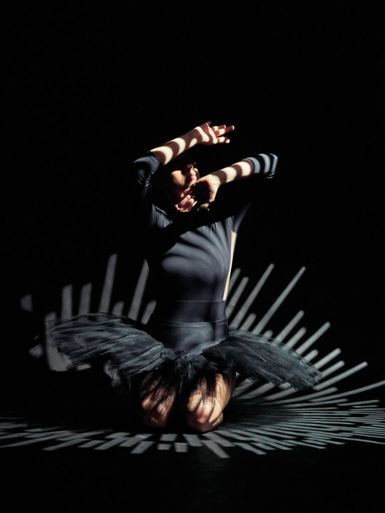 Danseuse accroupie, visage dans les mains, avec un éclairage créant des ombres et lignes graphiques.
