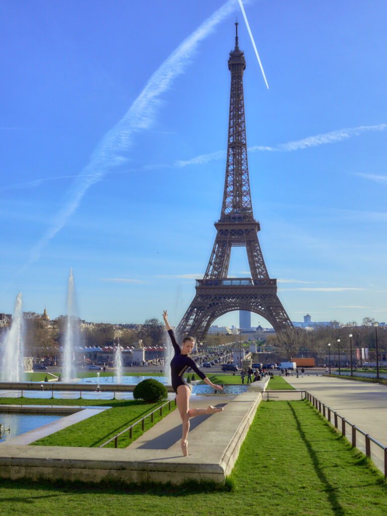 Lola (@lolite.danse) en pose d'attitude sur une jambe, sur pointes, devant les bassins et les jets d'eau des jardins du Trocadéro à Paris.