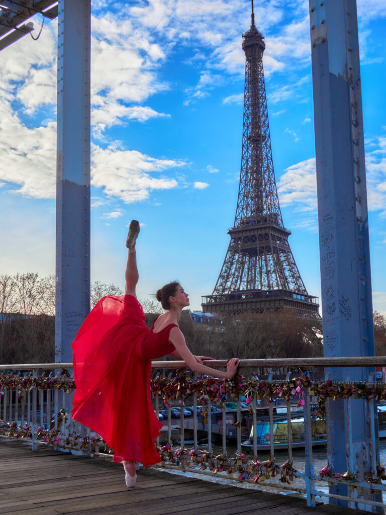 Daria effectuant un grand écart à 180 degrés en s'appuyant sur la rambarde d'une passerelle ornée de cadenas, avec la Tour Eiffel majestueuse en fond.