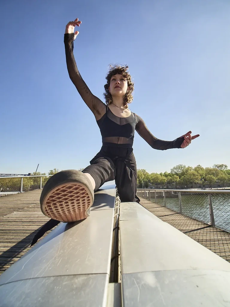 Danseuse en tenue résille, jambe levée sur une rambarde, passerelle Simone de Beauvoir.