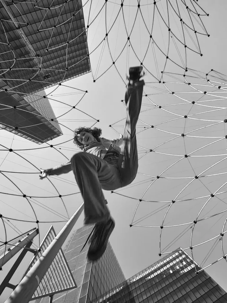 Danseuse en tenue denim en équilibre inversé, jambe levée, sous une structure métallique en filet à la bibliothèque Francois Mitterrand.