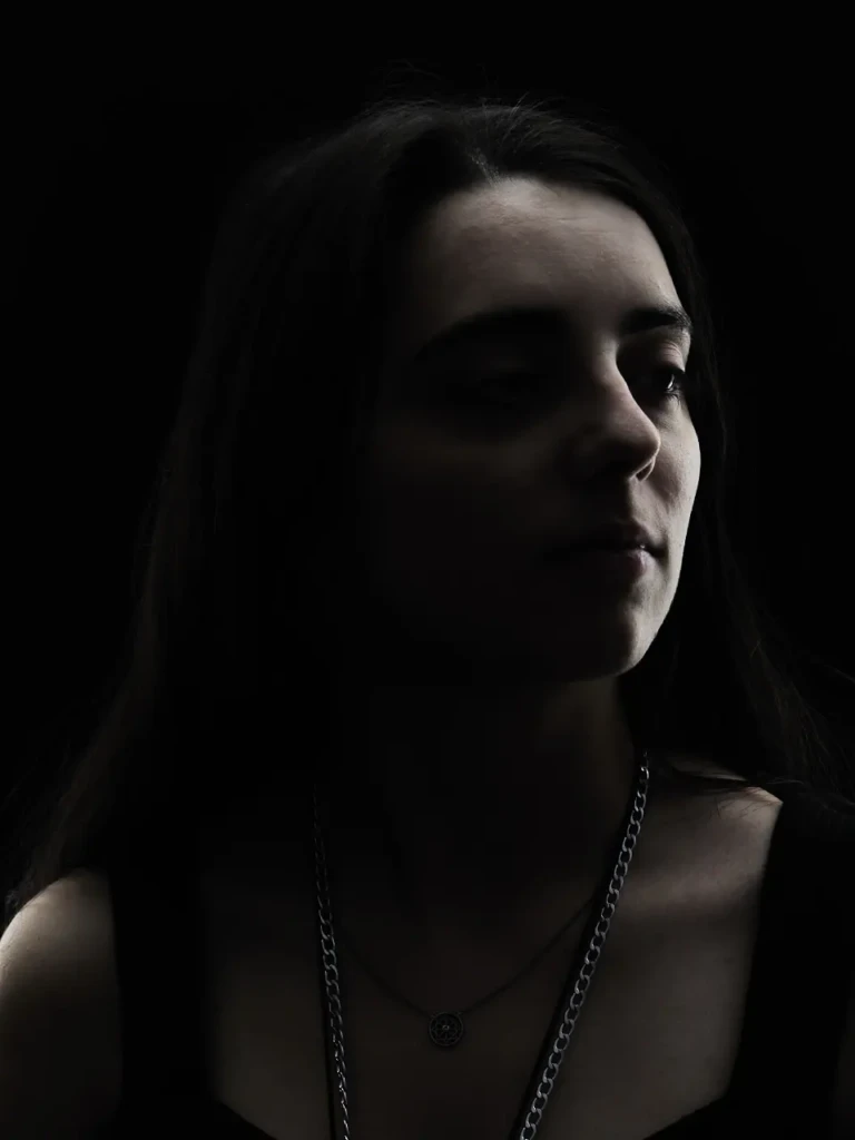 Portrait de femme en lumière sculptée sur fond noir, visage émergeant de l'obscurité.