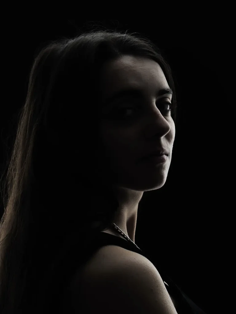Portrait de femme regardant par-dessus l'épaule, éclairage dramatique sur fond noir.