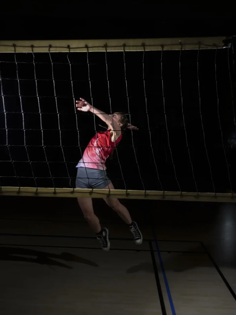 Joueuse de volley en plein smash au filet, suspendue en l'air, fond noir.