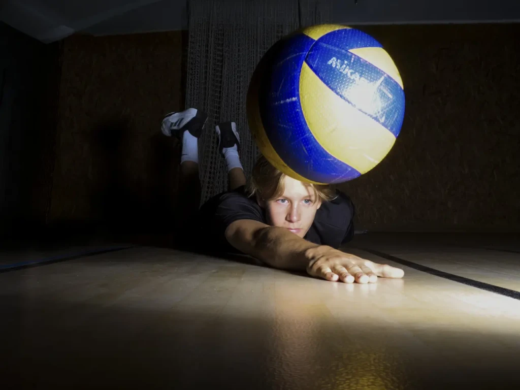 Gros plan sur un ballon de volley flou au premier plan, joueur allongé au sol en arrière-plan.