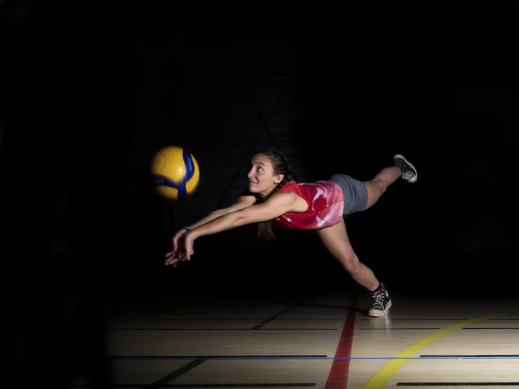 Joueuse de volley plongeant pour rattraper le ballon, fond noir, éclairage studio.