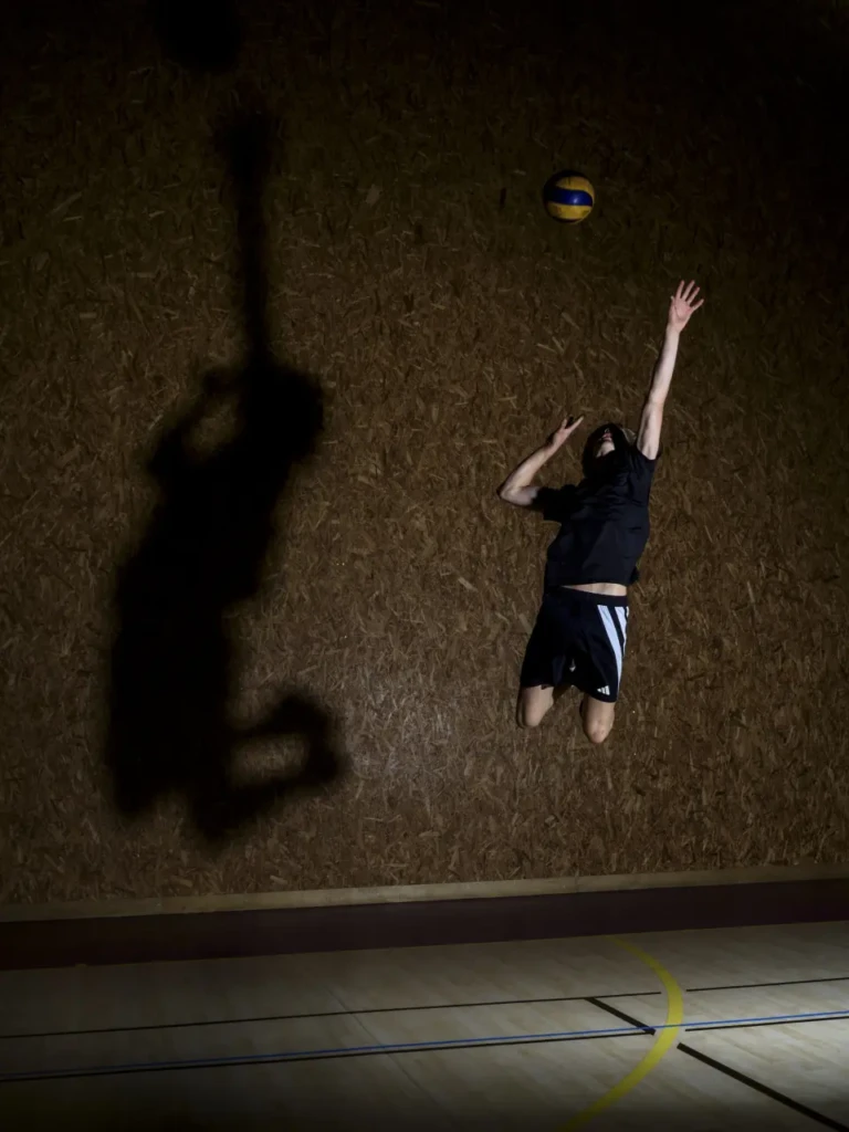 Joueur de volley sautant pour un service, ombre projetée sur un mur en arrière-plan.