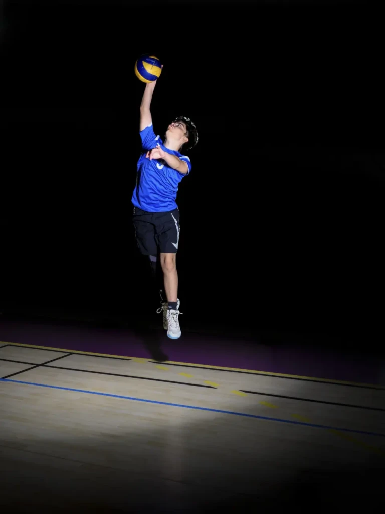 Joueur de volley en plein saut vertical pour un smash, ballon en main, fond noir.