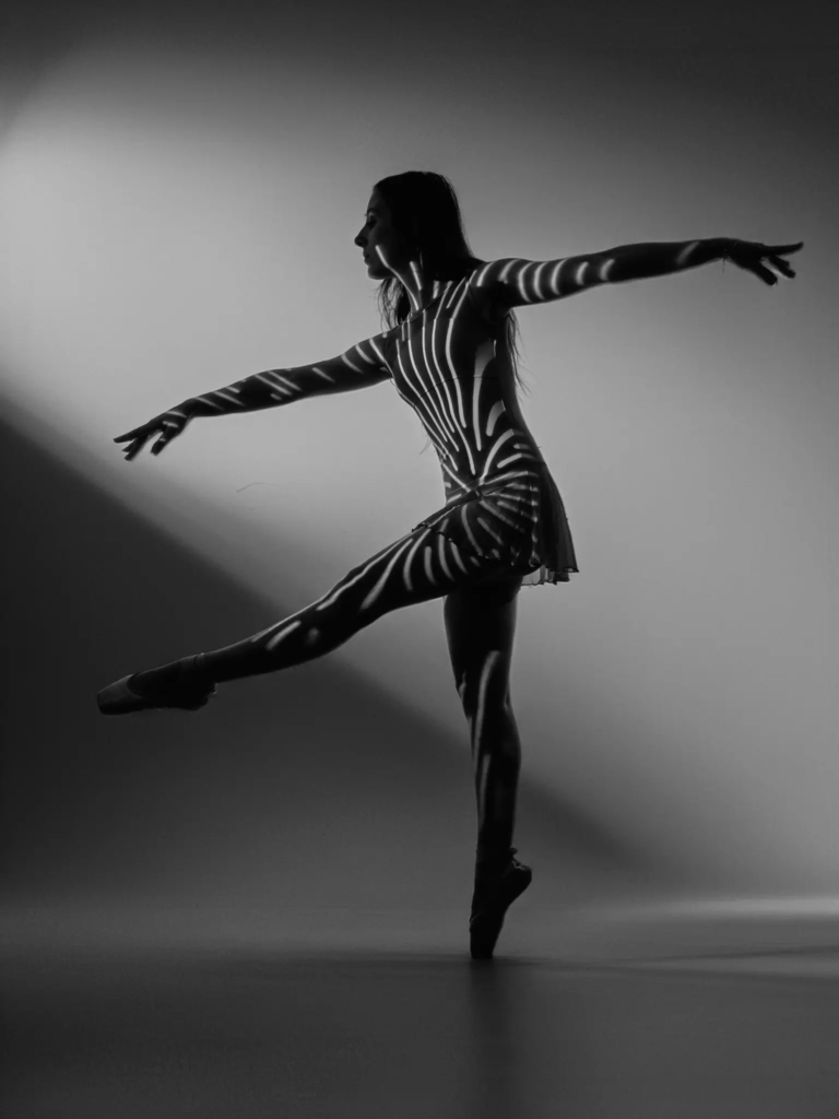 Danseuse en arabesque, motif de lumière en rayures sur le corps, photo danse studio